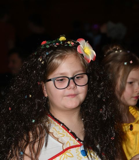 Ein junges Mädchen mit Brille und einer Blume im Haar posiert für ein Foto bei einer festlichen Veranstaltung.