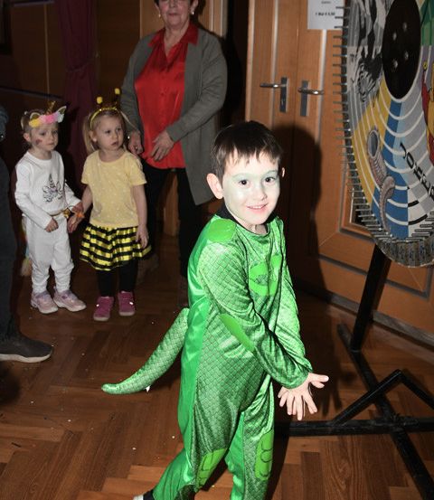 Ein Junge in einem grünen Kostüm posiert für ein Foto mit zwei Mädchen und einer erwachsenen Frau in einem Raum.