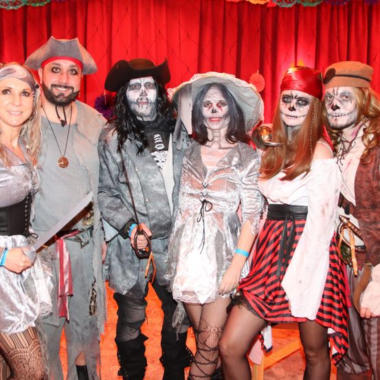 Eine Gruppe von Menschen in Piratenkostümen posiert für ein Foto vor einem roten Vorhang. Jede Person hat ein einzigartiges Kostüm und einige tragen Gesichtsbemalung.