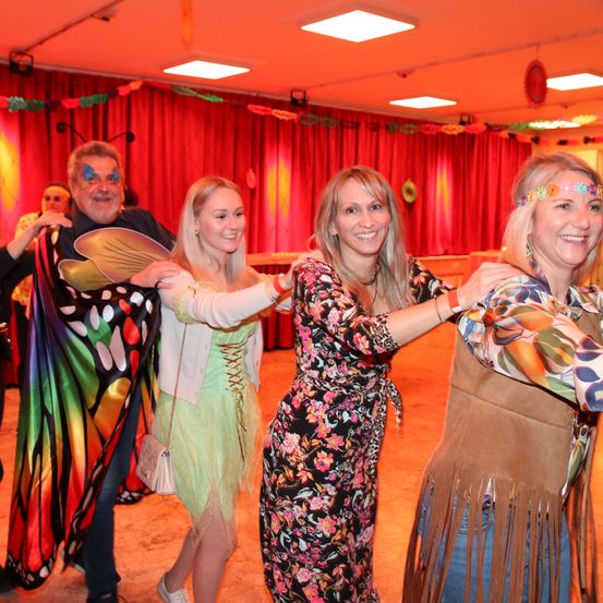 Vier Erwachsene posieren für ein Foto in einem Partysaal. Sie tragen Kostüme und lächeln.