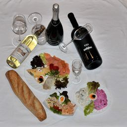 Ein Tisch mit verschiedenen Gerichten, einschließlich Brot, Fisch und Salaten, mit Weingläsern und Flaschen Champagner und Wein.