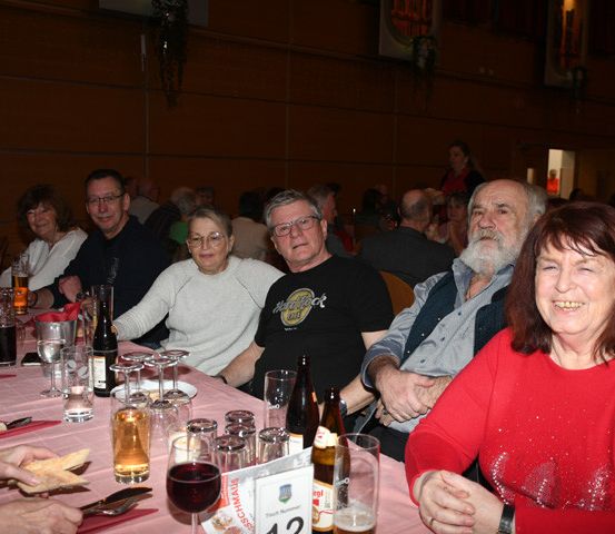 Eine Gruppe von Menschen sitzt an einem Tisch in einem Restaurant. Sie haben Wein, Bier und Wasser. Sie lächeln.