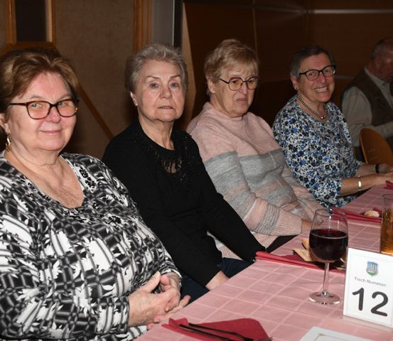 Vier ältere Frauen und ein älterer Mann sitzen an einem Tisch mit Getränken und Essen. Eine Frau mit Brille lächelt in die Kamera.