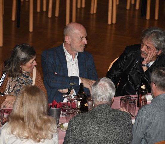 Eine Gruppe von Menschen sitzt um einen Tisch herum, wahrscheinlich in einem Restaurant. Sie scheinen miteinander zu sprechen.