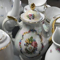 Eine Sammlung weißer Porzellantee-Sets mit Blumenmustern, auf einer grauen Oberfläche angeordnet. Jedes Stück zeigt kunstvolle Blumendesigns, einschließlich Teekannen, Tassen und Untertassen.