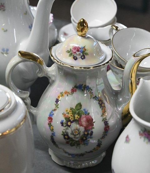 Eine Sammlung weißer Porzellantee-Sets mit Blumenmustern, auf einer grauen Oberfläche angeordnet. Jedes Stück zeigt kunstvolle Blumendesigns, einschließlich Teekannen, Tassen und Untertassen.