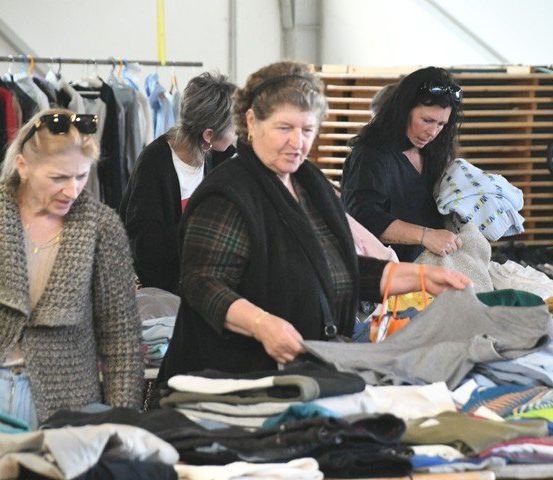 Eine Gruppe von Frauen sortiert Kleidung in einem Raum mit Kleiderstangen im Hintergrund.