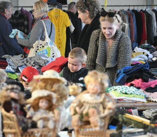 Ein Kleidermarkt mit mehreren Erwachsenen und Kindern beim Einkaufen, mit Spielzeug und Kleidung im Angebot.