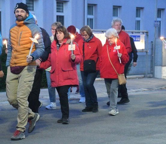 Eine Gruppe von Menschen in Jacken geht mit brennenden Kerzen in der Hand die Straße entlang.