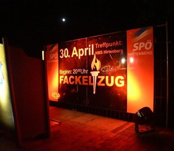 Ein großer beleuchteter Schild mit einer Fackel und Text, und ein Mond am Himmel. Das Schild ist für eine Veranstaltung am 30. April.