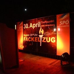 Ein großer beleuchteter Schild mit einer Fackel und Text, und ein Mond am Himmel. Das Schild ist für eine Veranstaltung am 30. April.
