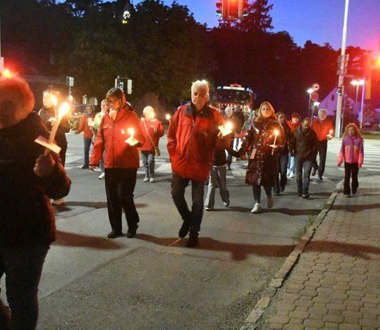 Eine Gruppe von Menschen in roten Jacken geht mit brennenden Kerzen auf einer Straße bei Nacht.