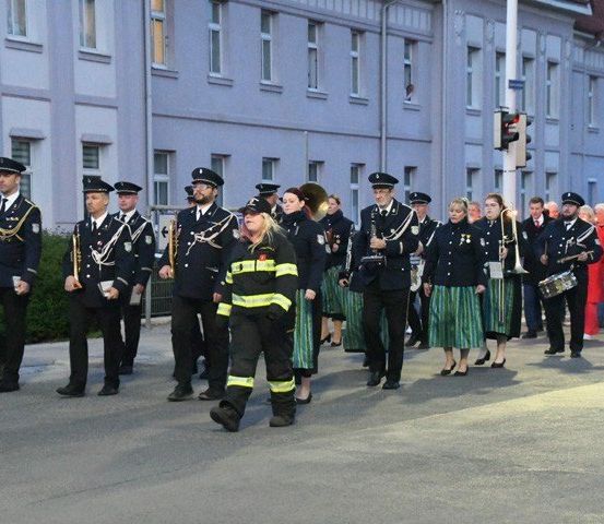 Eine Gruppe uniformierter Personen, darunter Feuerwehrleute, marschiert mit Musikinstrumenten in einem Stadtparade.