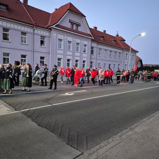 Ein Umzug mit Menschen in Rot, die Kerzen halten, vor einem Gebäude mit roten Dächern und Fenstern.
