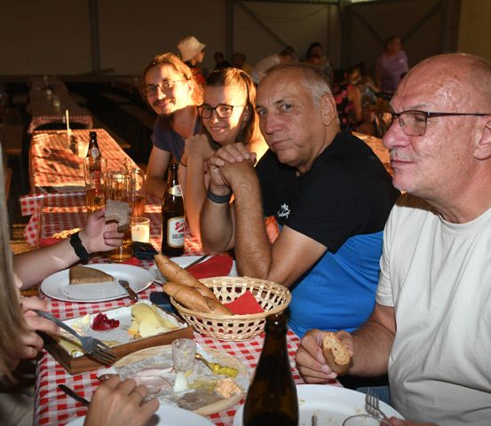Eine Gruppe von Menschen sitzt um einen Tisch in einem Restaurant und genießt eine Mahlzeit mit Brot, Käse und Getränken.
