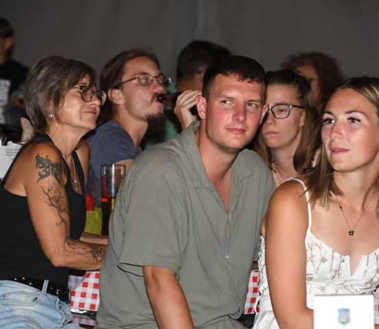 Eine Gruppe von Menschen sitzt an einem Tisch, einige trinken und andere schauen etwas an. Der Tisch hat eine rot-weiß karierte Tischdecke.
