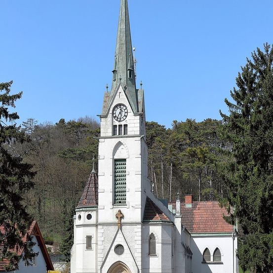Eine weiße Kirche mit Kirchturm und Uhr steht inmitten eines üppigen grünen Waldes.
