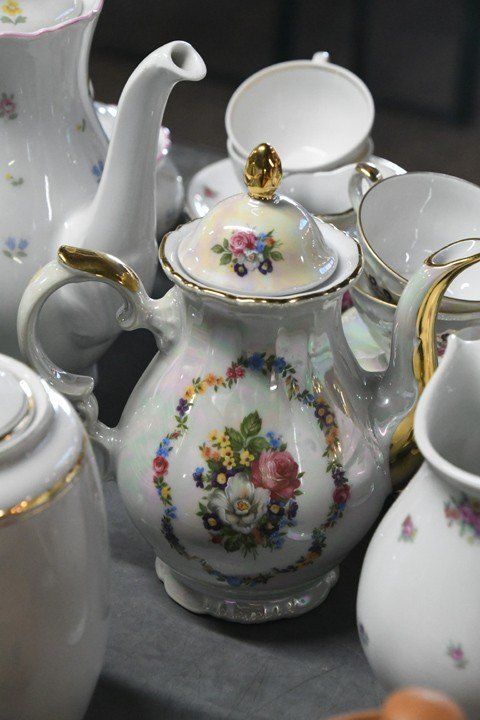 A collection of white porcelain teapots and cups with floral designs on a gray surface.