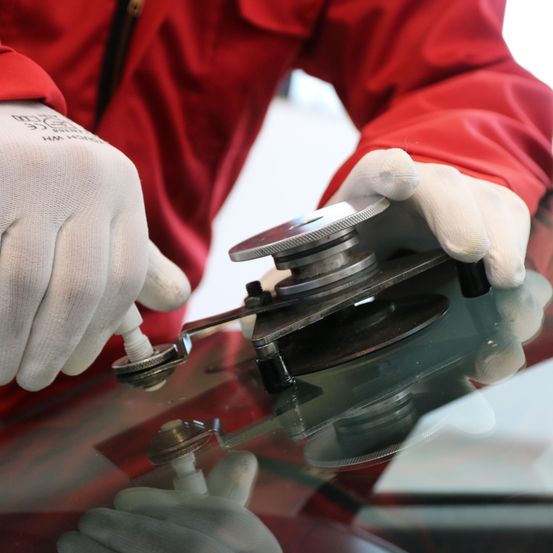 Eine Person in einem roten Jacke und weißen Handschuhen arbeitet mit einem Werkzeug an einer Glasscheibe.