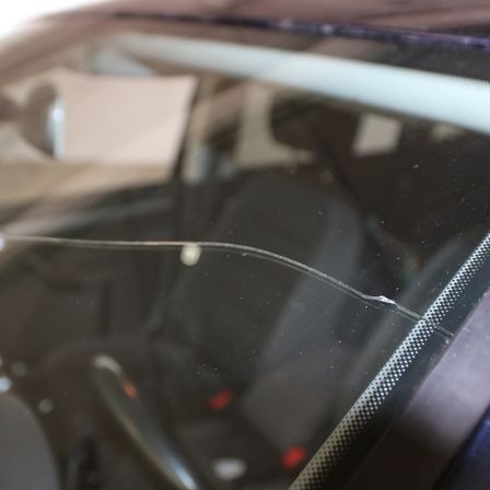 Eine Nahaufnahme einer gerissenen Windschutzscheibe eines Autos mit einem Metallrahmen darum.