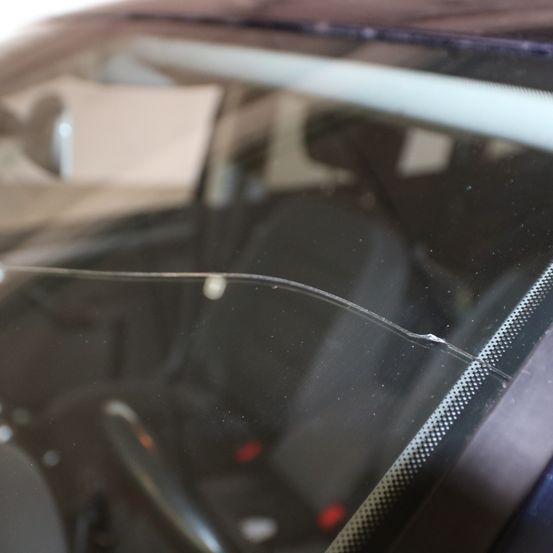 Eine Nahaufnahme einer gerissenen Windschutzscheibe eines Autos mit einem Metallrahmen darum.