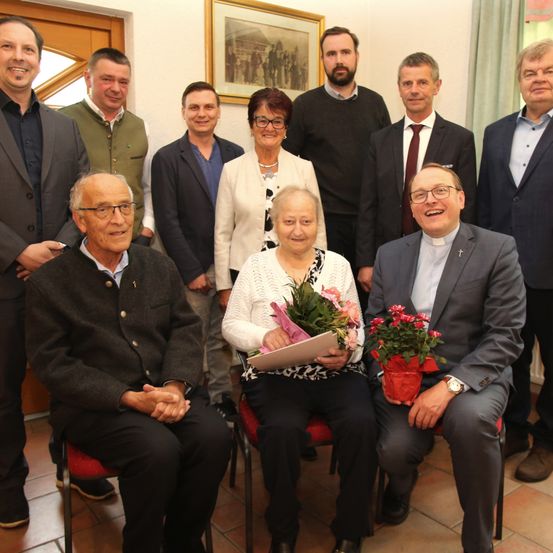 Eine Gruppe von Menschen posiert für ein Foto, einige sitzen auf Stühlen und andere stehen hinter ihnen, sie alle lächeln und schauen in die Kamera.