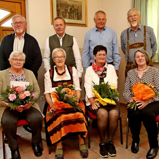 Eine Gruppe älterer Menschen posiert für ein Foto und hält Blumen. Eine von ihnen trägt ein traditionelles Kleid.