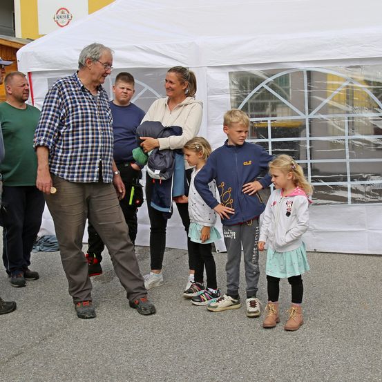 Eine Gruppe von Menschen steht vor einem Zelt. Ein Mann und eine Frau mit Kindern stehen vorne.