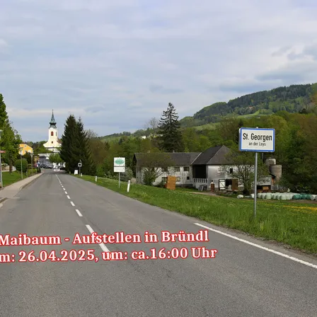 Eine Straße, die zu einem Dorf mit einer Kirche, Bergen im Hintergrund und einem Schild, das St. Georgen an der Leys anzeigt. Das Datum und die Uhrzeit des Bildes sind der 26. April 2025, etwa um 16:00 Uhr.