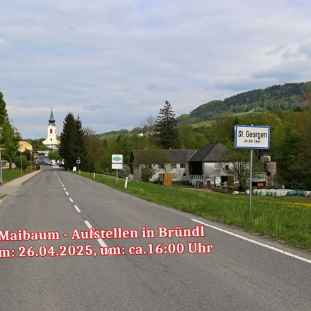 Eine Straße, die zu einem Dorf mit einer Kirche, Bergen im Hintergrund und einem Schild, das St. Georgen an der Leys anzeigt. Das Datum und die Uhrzeit des Bildes sind der 26. April 2025, etwa um 16:00 Uhr.
