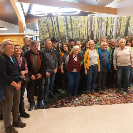 Eine Gruppe älterer Menschen steht vor einer großen Wandmalerei eines Waldes. Sie alle lächeln und scheinen für ein Foto zu posieren.