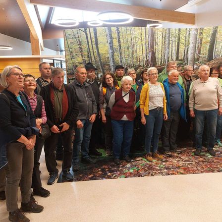 Eine Gruppe älterer Menschen steht vor einer großen Wandmalerei eines Waldes. Sie alle lächeln und scheinen für ein Foto zu posieren.