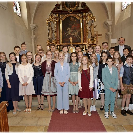 Eine Gruppe von Kindern und Jugendlichen in formeller Kleidung posiert in einer Kirche, mit einem kunstvollen Altar im Hintergrund.