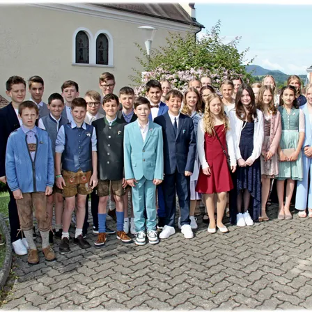 Eine Gruppe von Schülern in traditioneller Kleidung steht vor einem Gebäude mit Bäumen und Bergen im Hintergrund.