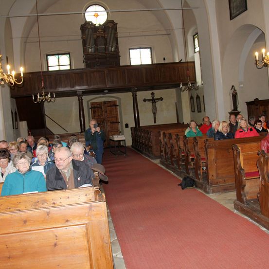 Eine Gemeinde versammelt sich in einer Kirche, mit gefüllten Bänken auf beiden Seiten, einem Altar im Blick und einer Person, die am hinteren Ende ein Foto macht.