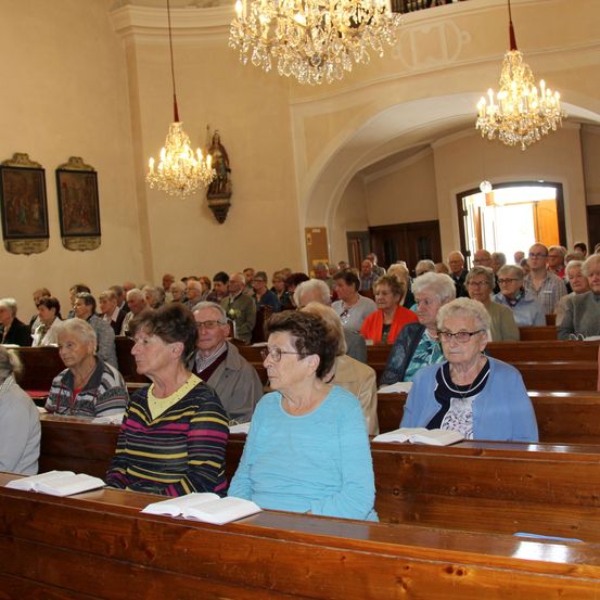 Eine Gemeinde älterer Erwachsener in einer Kirche mit hölzernen Kirchenbänken, Büchern in den Händen und Kronleuchtern an der Decke.