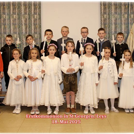 Eine Gruppe junger Kinder in weißen Kleidern, die Kerzen halten, posiert für ein Foto, wahrscheinlich für eine Erstkommunion. Das Bild ist auf den 18. Mai 2025 datiert.