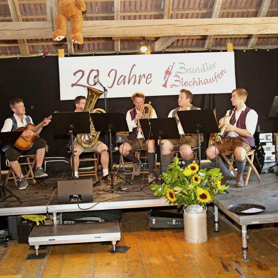 Eine Gruppe Musiker spielt Instrumente auf der Bühne. Dahinter befindet sich ein Banner, das 20 Jahre Blechhaufen feiert.