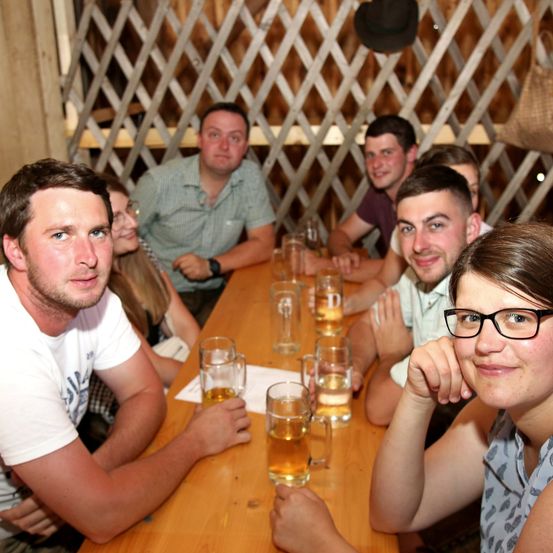 Eine Gruppe von Menschen sitzt um einen Tisch in einer rustikalen Bar. Sie lächeln und scheinen ihre Getränke zu genießen.