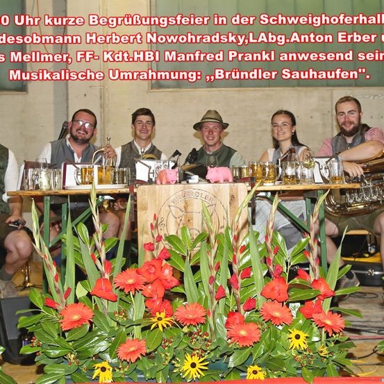 Gruppenfoto von Musikern mit roten Blumen im Vordergrund. Die Bildunterschrift lautet 'Kurze Begrüßungsfeier um 10 Uhr in der Schweighoferhalle'.