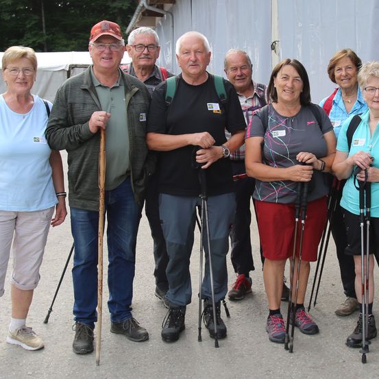Eine Gruppe von Erwachsenen, alle mit Trekkingstöcken, stehen zusammen draußen in einem offenen Bereich und lächeln für ein Foto.