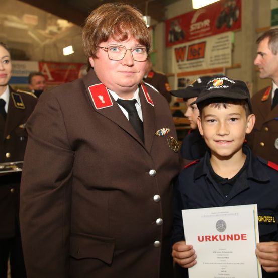 Eine Frau und ein Junge in Uniform stehen lächelnd zusammen. Der Junge hält ein Zertifikat, und sie sind von anderen in Uniform umgeben.