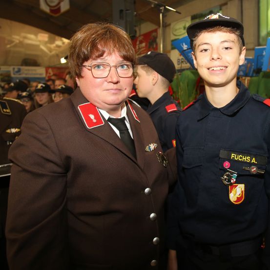 Eine Frau und ein Junge in Uniform stehen nebeneinander, mit anderen Menschen in Uniform dahinter.