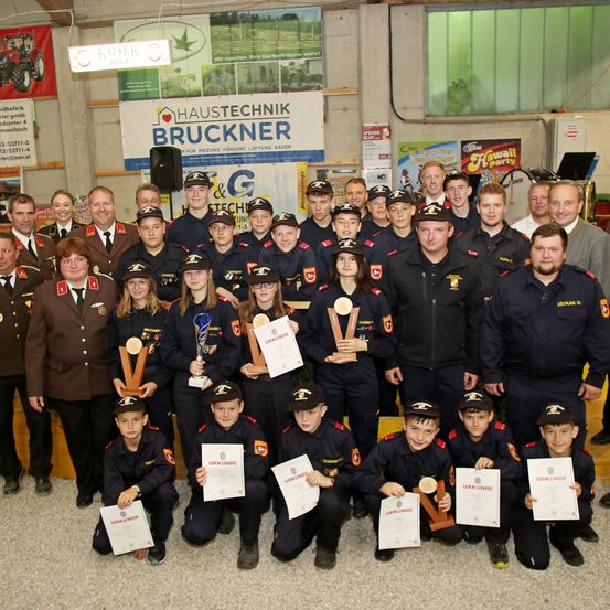 Eine Gruppe junger Menschen in Uniformen posiert für ein Foto und hält Auszeichnungen und Urkunden in den Händen. Sie befinden sich in einem Raum mit Plakaten an den Wänden.