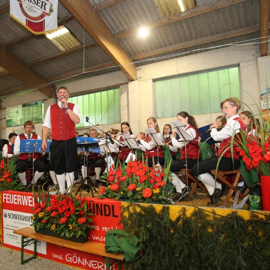 Eine Band auf der Bühne mit einem Sänger vorn, umgeben von Blumen. Die Bühne hat einen roten und gelben Hintergrund mit Text.