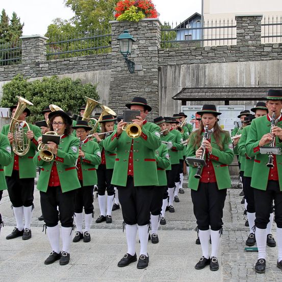Eine Blaskapelle in grünen Uniformen spielt im Freien, mit Musikern, die Trompeten, Posaunen und Klarinetten in einer Reihe spielen.