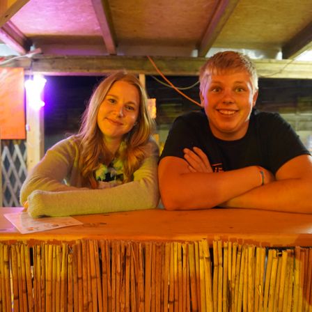 Zwei junge Leute lächeln und posieren für ein Foto an einer Holztheke mit Bambuszäunen davor.