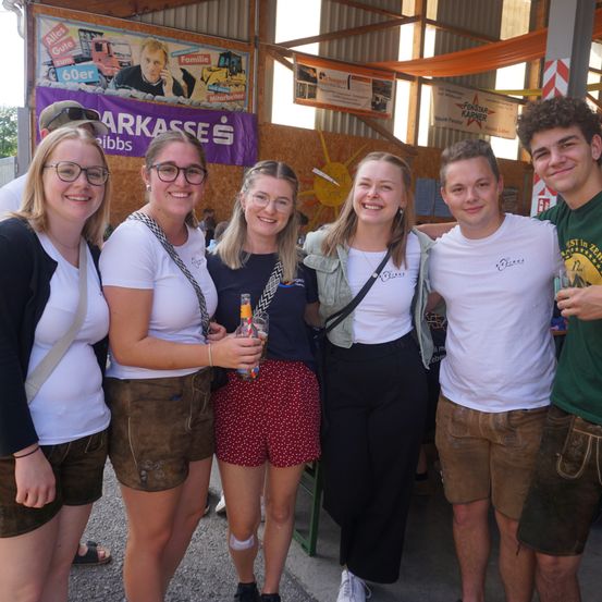 Eine Gruppe von Menschen in traditioneller deutscher Kleidung lächelt und posiert für ein Foto bei einer Veranstaltung im Freien.