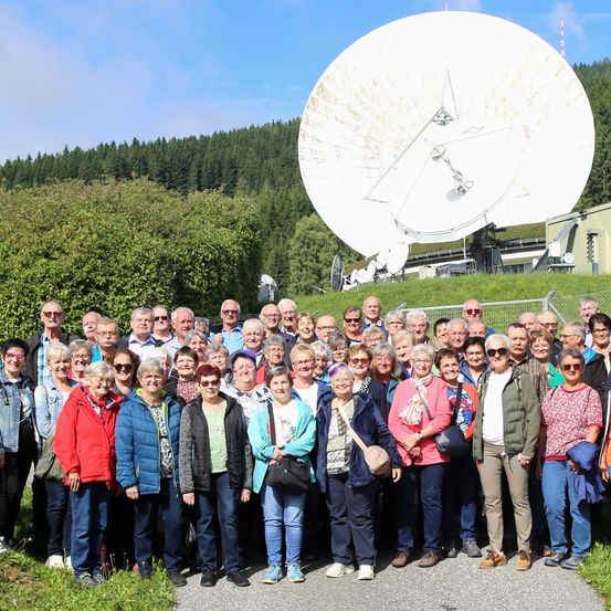 Eine Gruppe von Menschen in passenden Outfits posiert für ein Foto vor einer großen Satellitenschüssel.