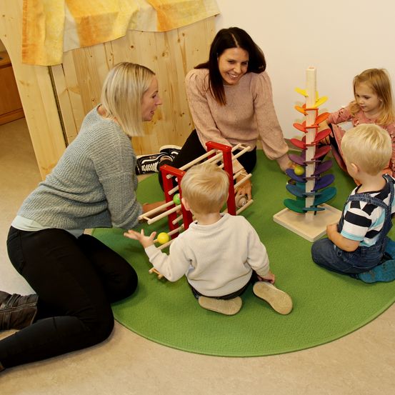 Eine Gruppe von Kindern spielt mit Spielzeug in einer Kindertagesstätte. Ein Kind spielt mit einem Ball und ein anderes Kind mit einem Spielzeug.